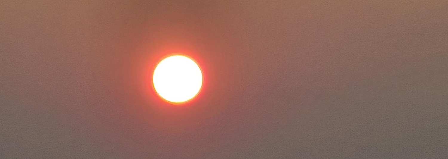A hazy red sun burning through smoke-coloured sky
