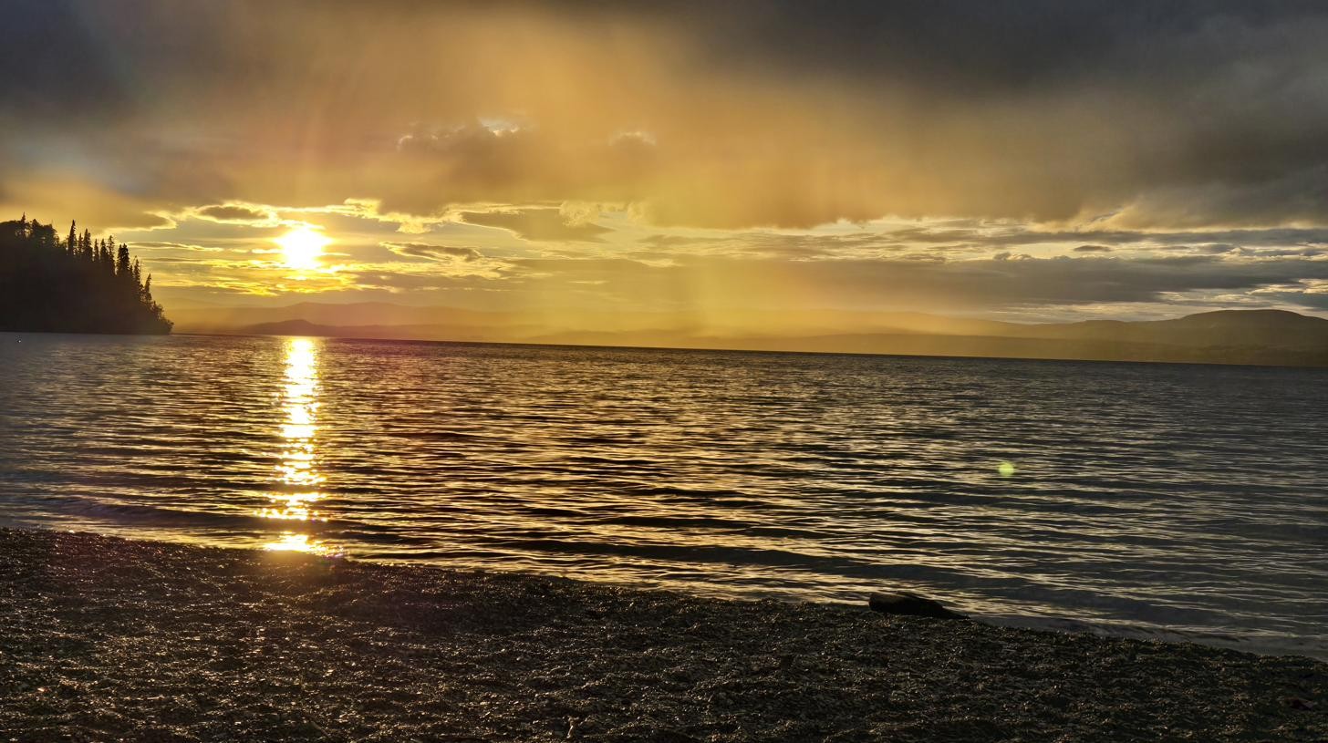 Storm clouds and golden sunset light sharing the same sky over a lake