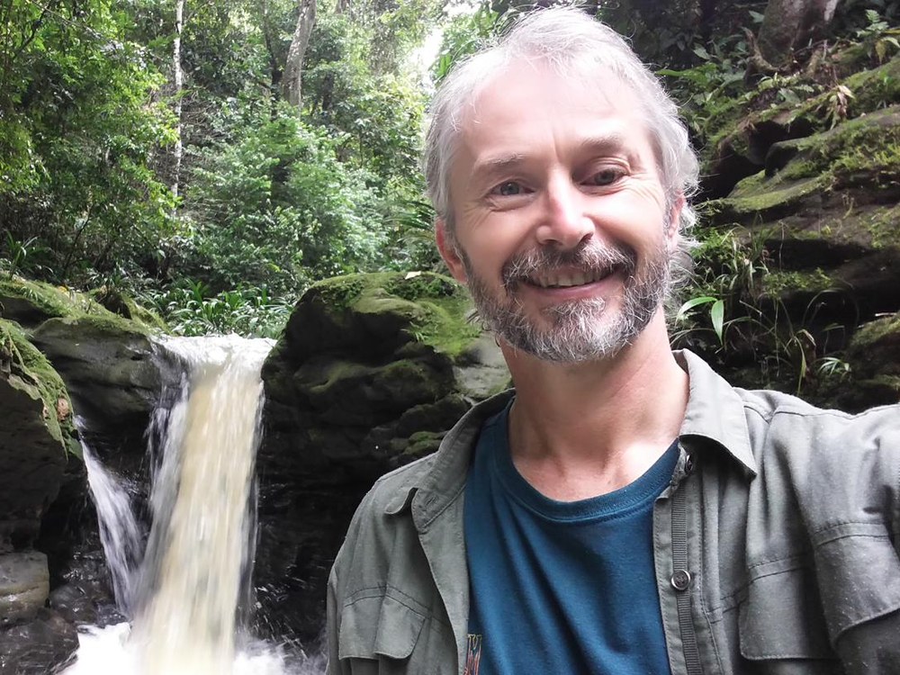 Todd Blattner smiling beside a small waterfall in a green forest