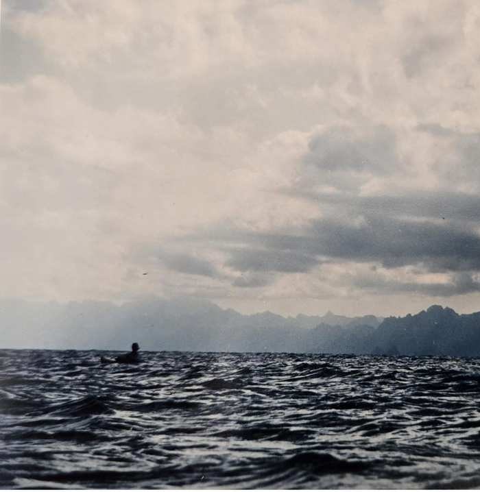 A tiny figure alone in a vast grey ocean, mountains in the distance
